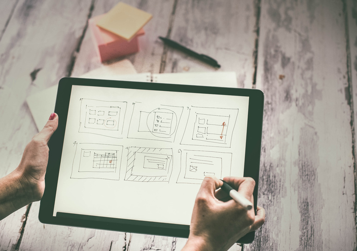 Hands sketching a website layout on a digital tablet, meant to illustrate a UX Designer working to create a layout with web accessibility and inclusive design in mind.