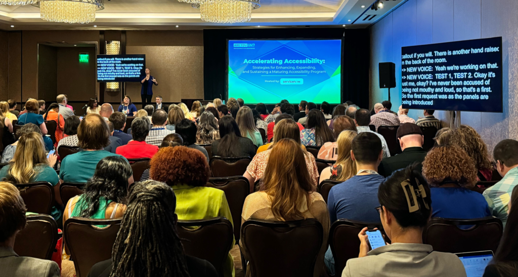 350 folks seated in a full conference room onlooking a panel discussion about Accelerating Accessibility