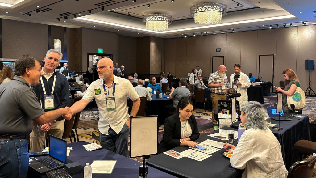 Dozens of attendees network together and explore the various lab stations. Seen in the foreground here, attendees chat with Rachael at the mobile station and Patrick at the lived experiences station.